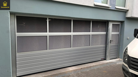 Tormeister24 Hörmann Fachhändler Techniker prüft ein geöffnetes Tiefgaragentor in einer Wohnanlage, gelb‑anthrazite Optik